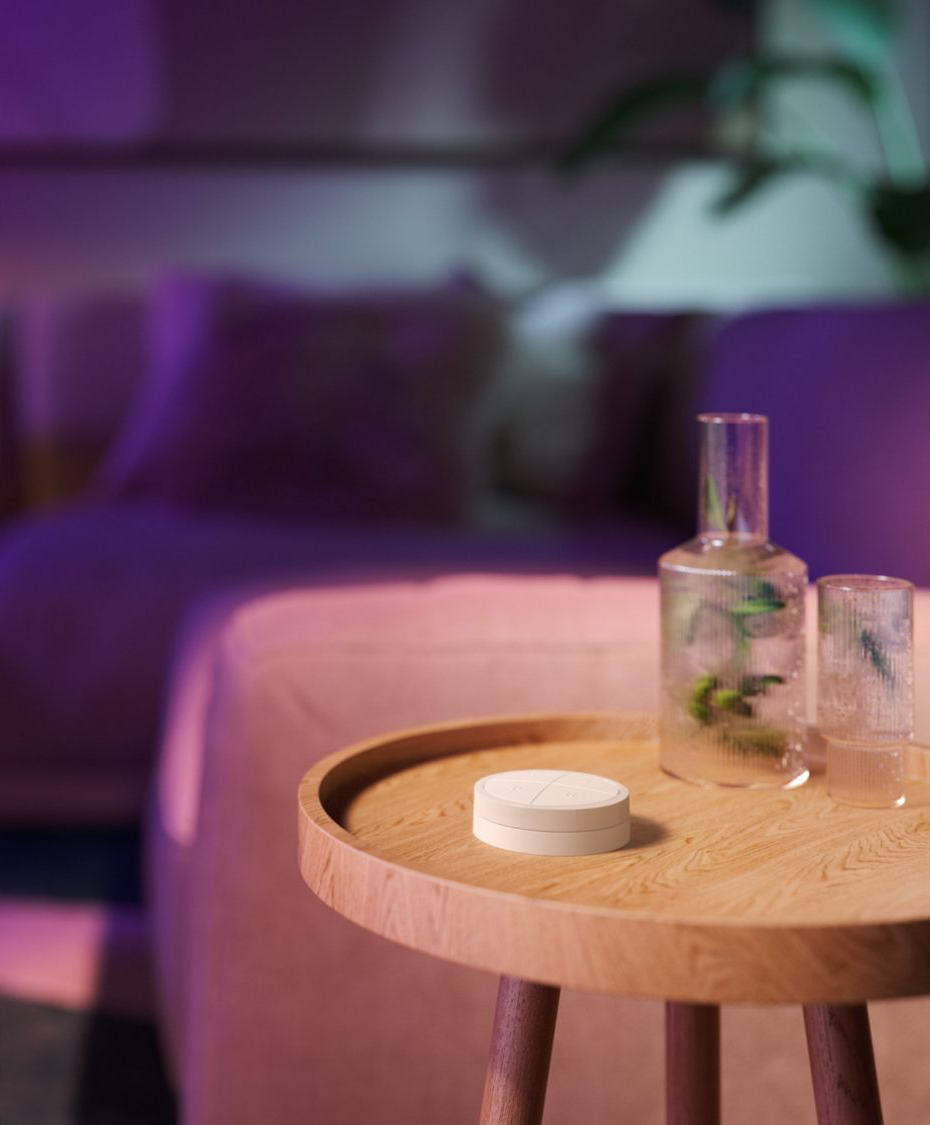 Un bouton intelligent blanc sur une table en bois avec un vase en verre et un verre à boire. Un canapé en arrière-plan.