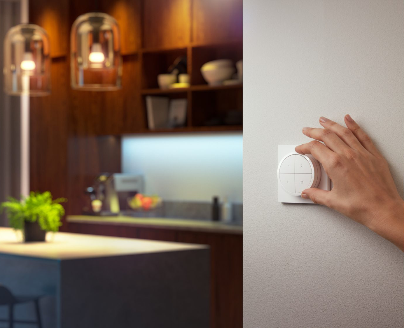 Une cuisine avec des lumières suspendues, une main réglant une commande domotique sur un mur blanc.