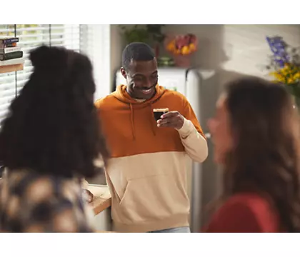 A man holding a cup, talking to two people.