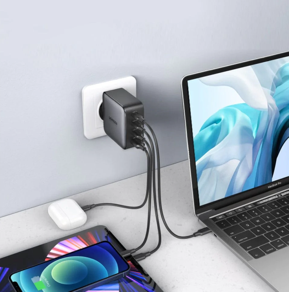 Adaptateur secteur noir avec plusieurs câbles de charge connectés à un ordinateur portable, une tablette et un téléphone.