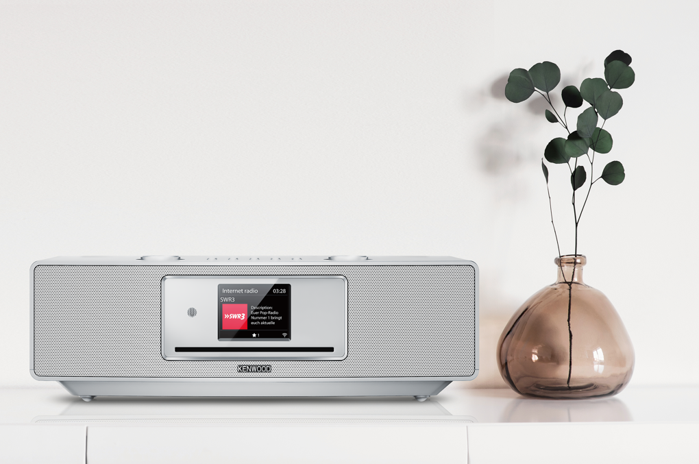 Kenwood Radio auf weißer Oberfläche. Vase mit Grünzeug rechts.