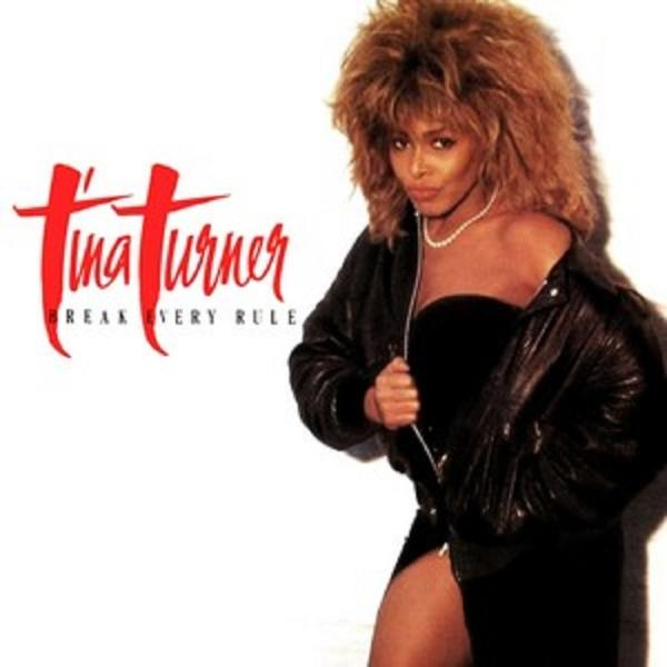 Tina Turner in een zwarte outfit. Ze draagt een zwarte jas en haar linkerbeen is zichtbaar.
