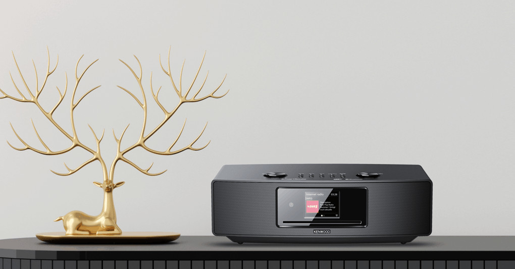Gold deer sculpture next to a Kenwood radio, black surface, white wall.