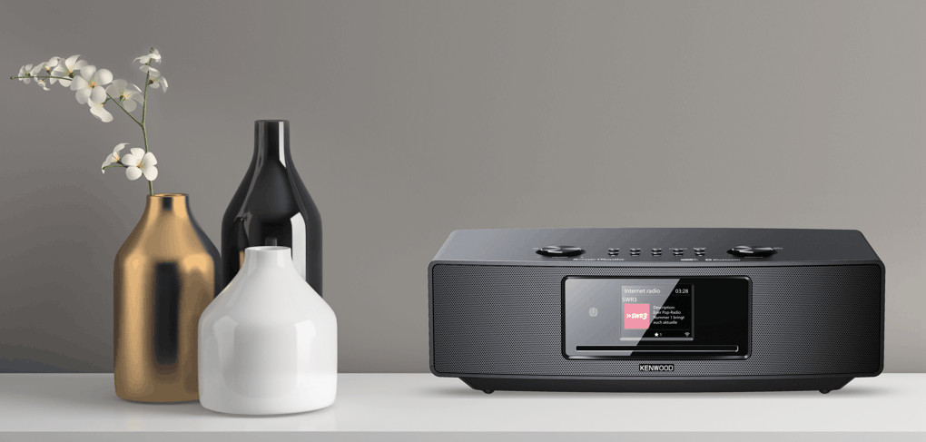 Stereo with a display showing information, flanked by vases with flowers on a shelf.