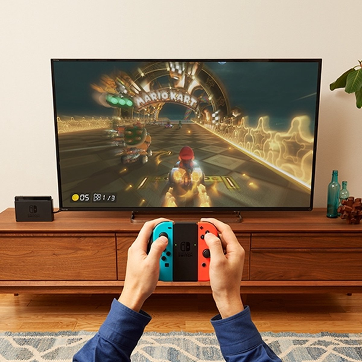 Hands holding a Nintendo Switch controller, playing Mario Kart on a TV.