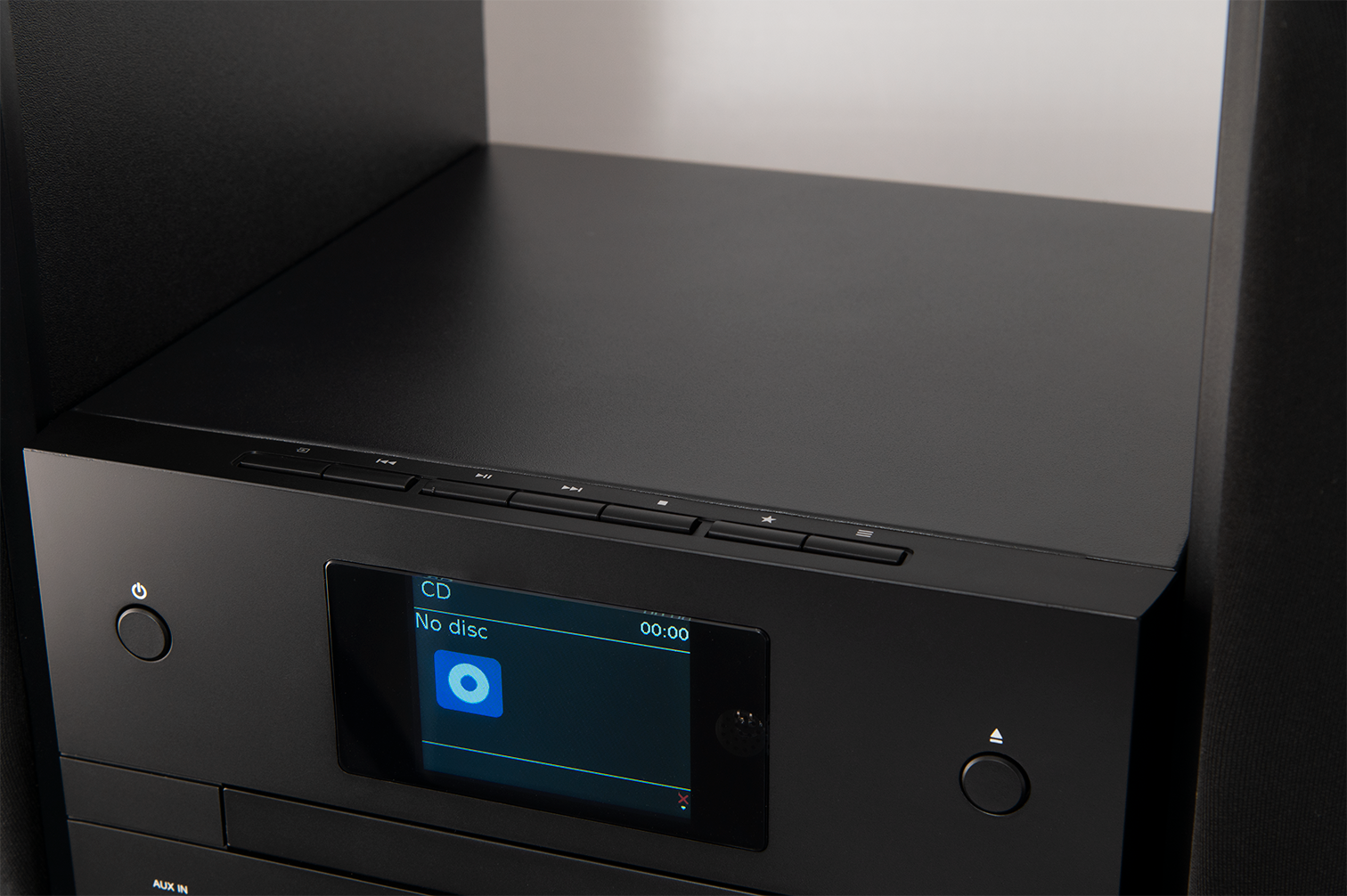 Un impianto stereo nero con un display che mostra 'No disc'. I pulsanti sono visibili. Su uno scaffale.