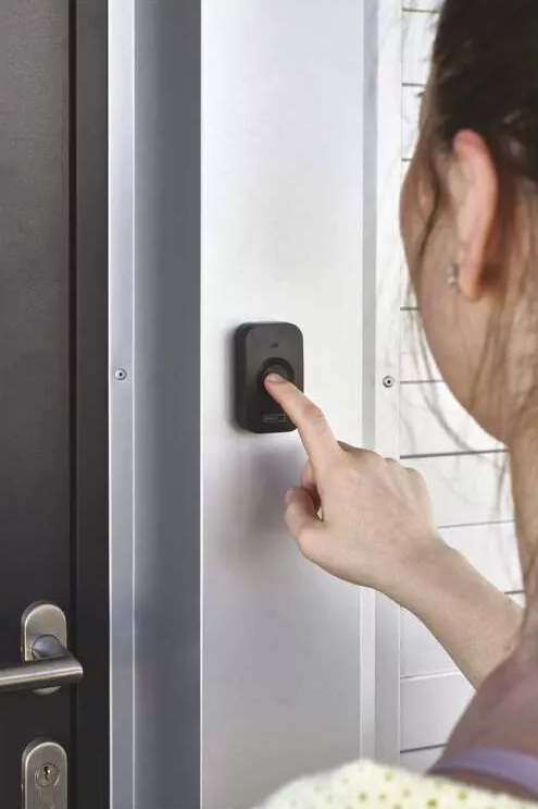 Egy nő ujja megnyomja a csengő gombot a falon.