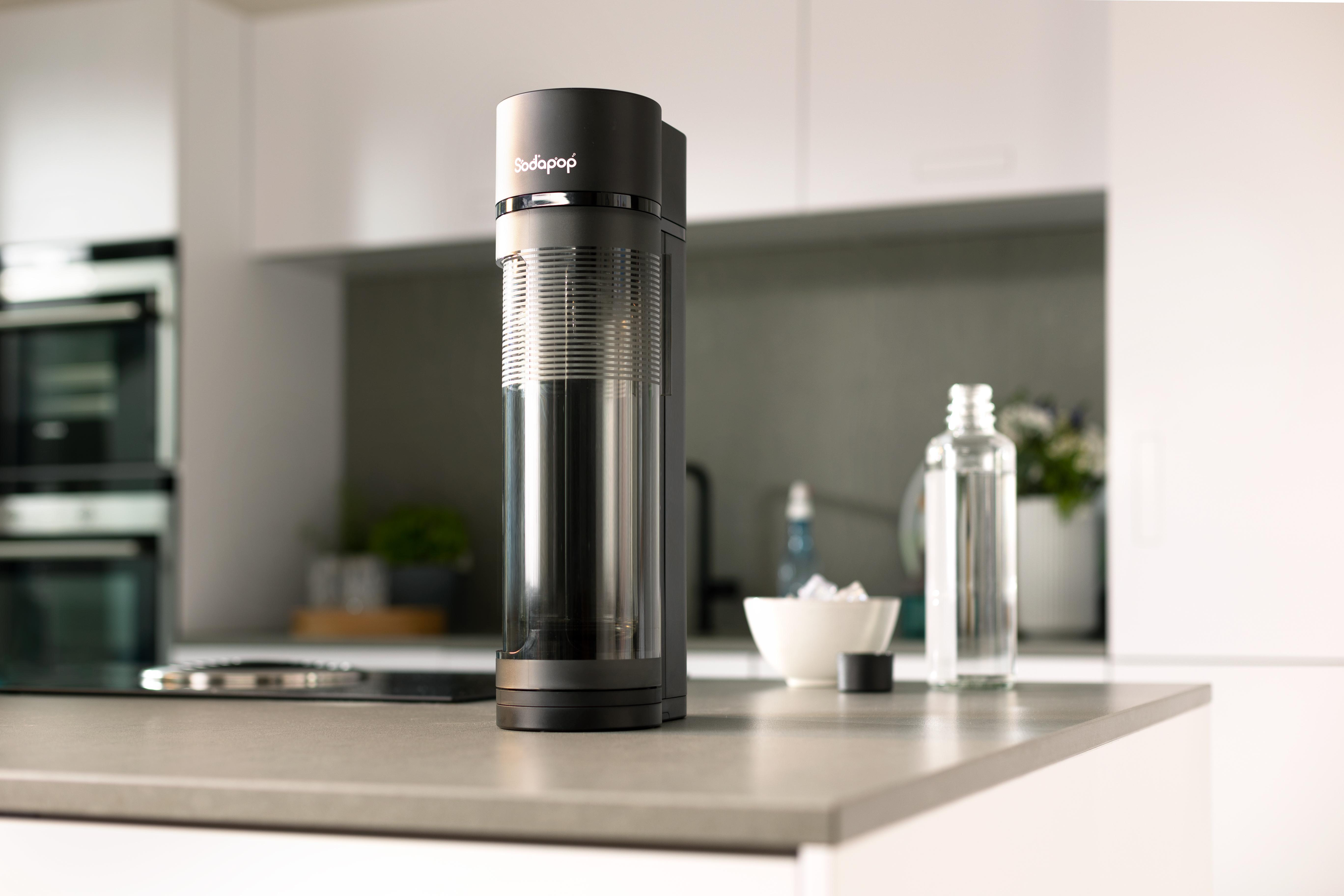 Schwarze SodaStream-Maschine auf einer Arbeitsplatte mit Eis und einer Wasserflasche.
