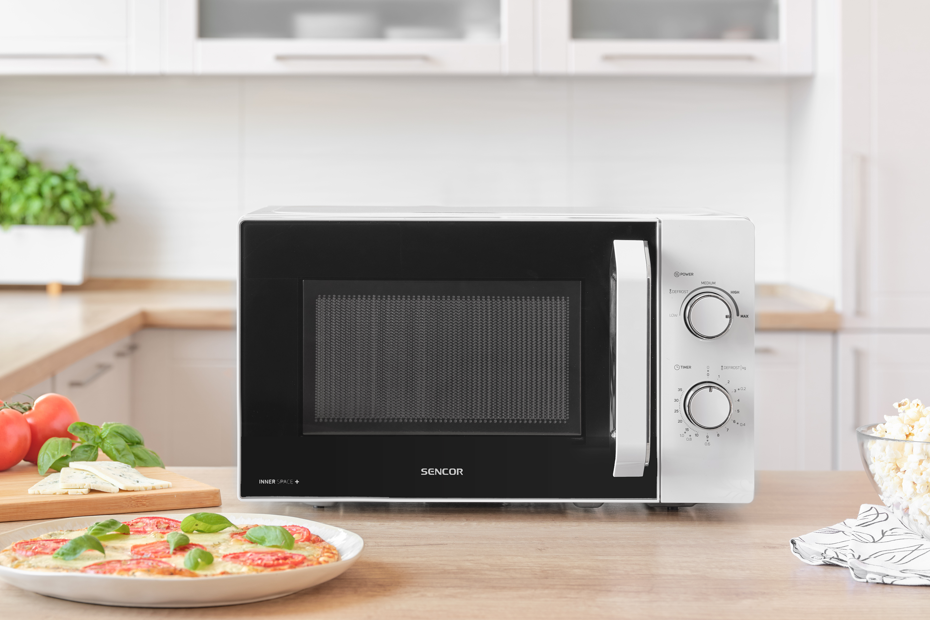 Egy mikrohullámú sütő fekete ajtóval, fehér kerettel és kezelőpanellel. Pizza és pattogatott kukorica látható.