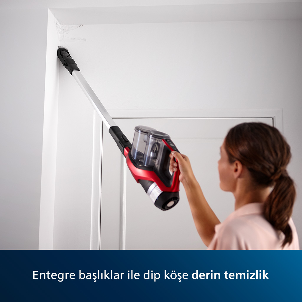 Beyaz bir duvarın köşesini temizlemek için kırmızı ve siyah kablosuz bir elektrikli süpürge kullanan bir kadın.