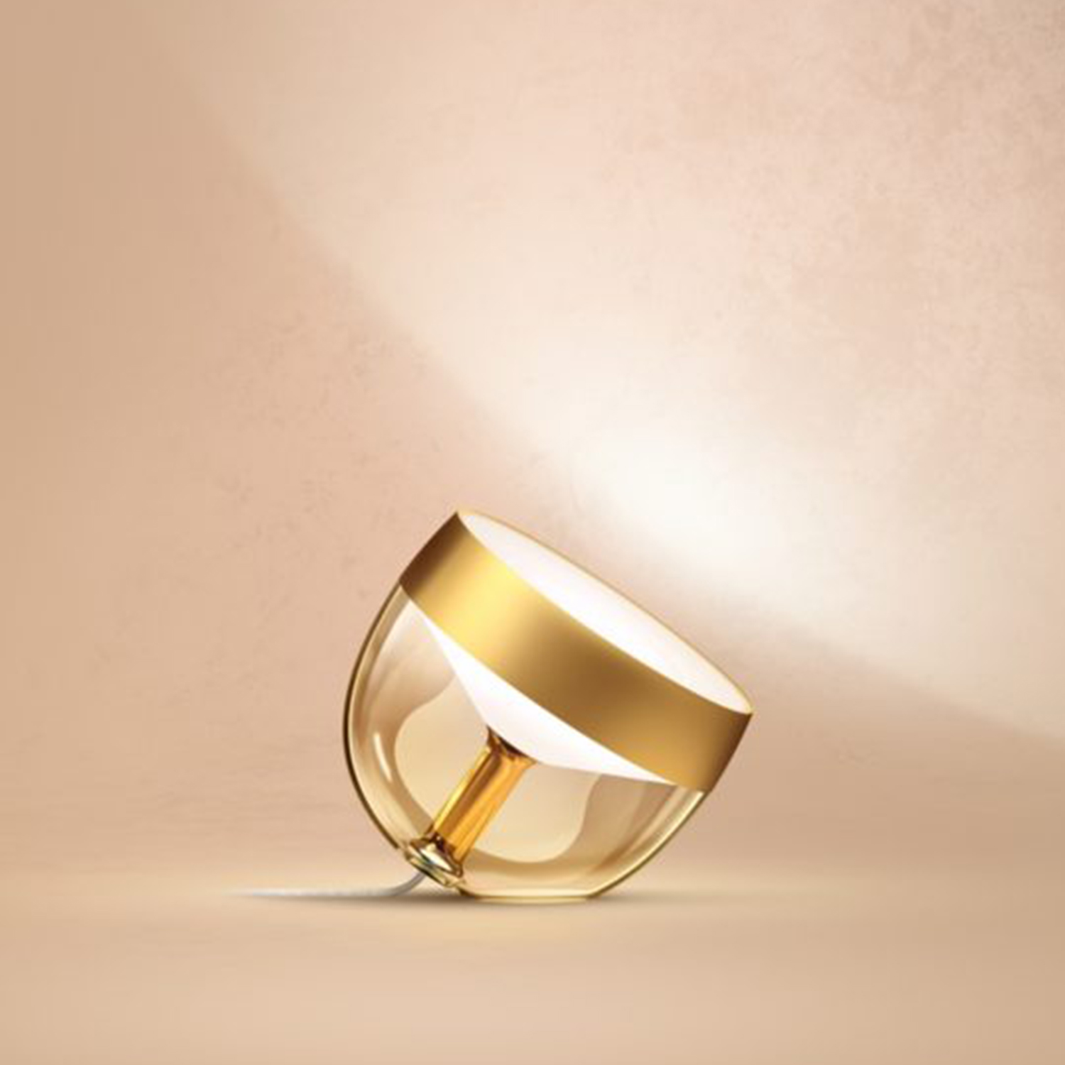 Un apparecchio di illuminazione in oro e vetro su sfondo beige. Vista angolata.