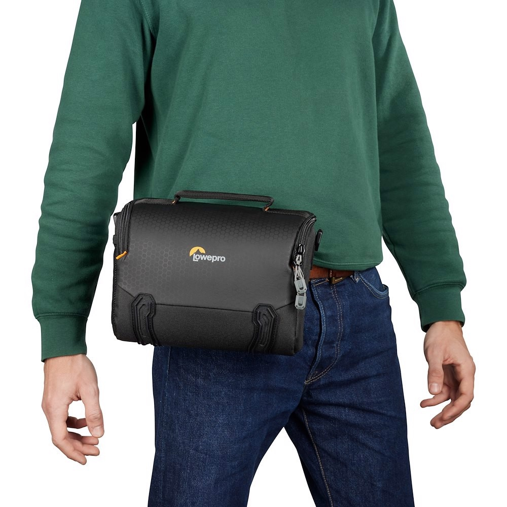 Una persona con una maglia verde e jeans ha una borsa fotografica Lowepro nera intorno alla vita.