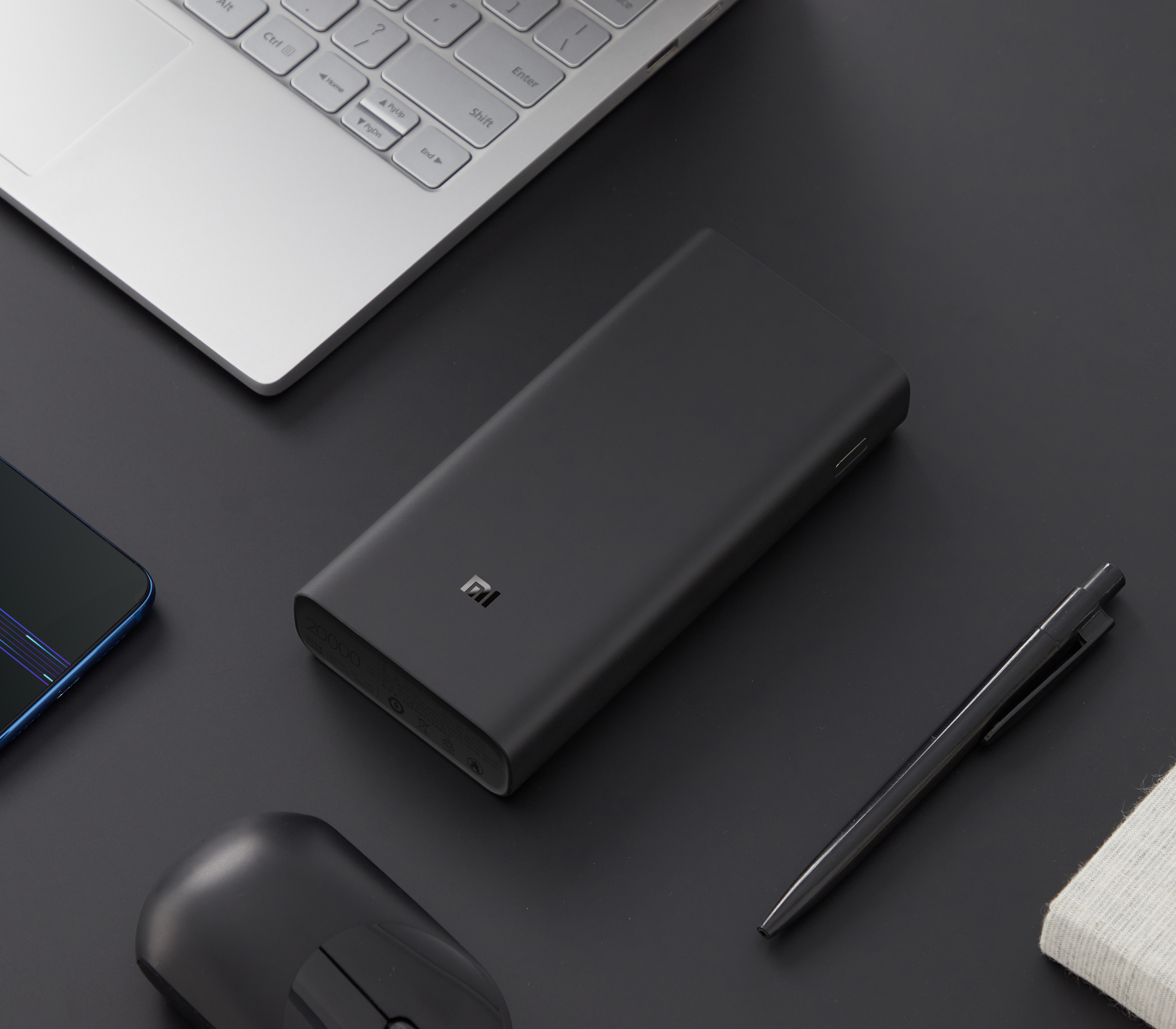 Power bank nero, laptop, mouse e penna su una superficie scura, che suggerisce un'impostazione dello spazio di lavoro.