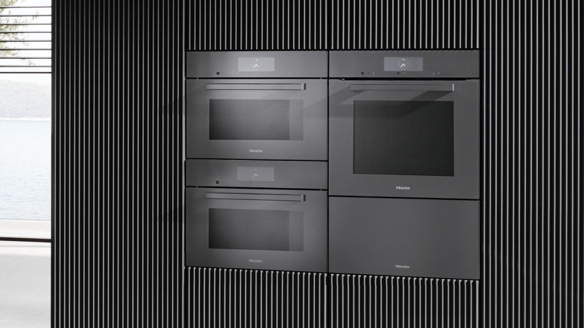 Schwarze Miele Einbauöfen und Mikrowelle an einer schwarzen Lamellenwand.