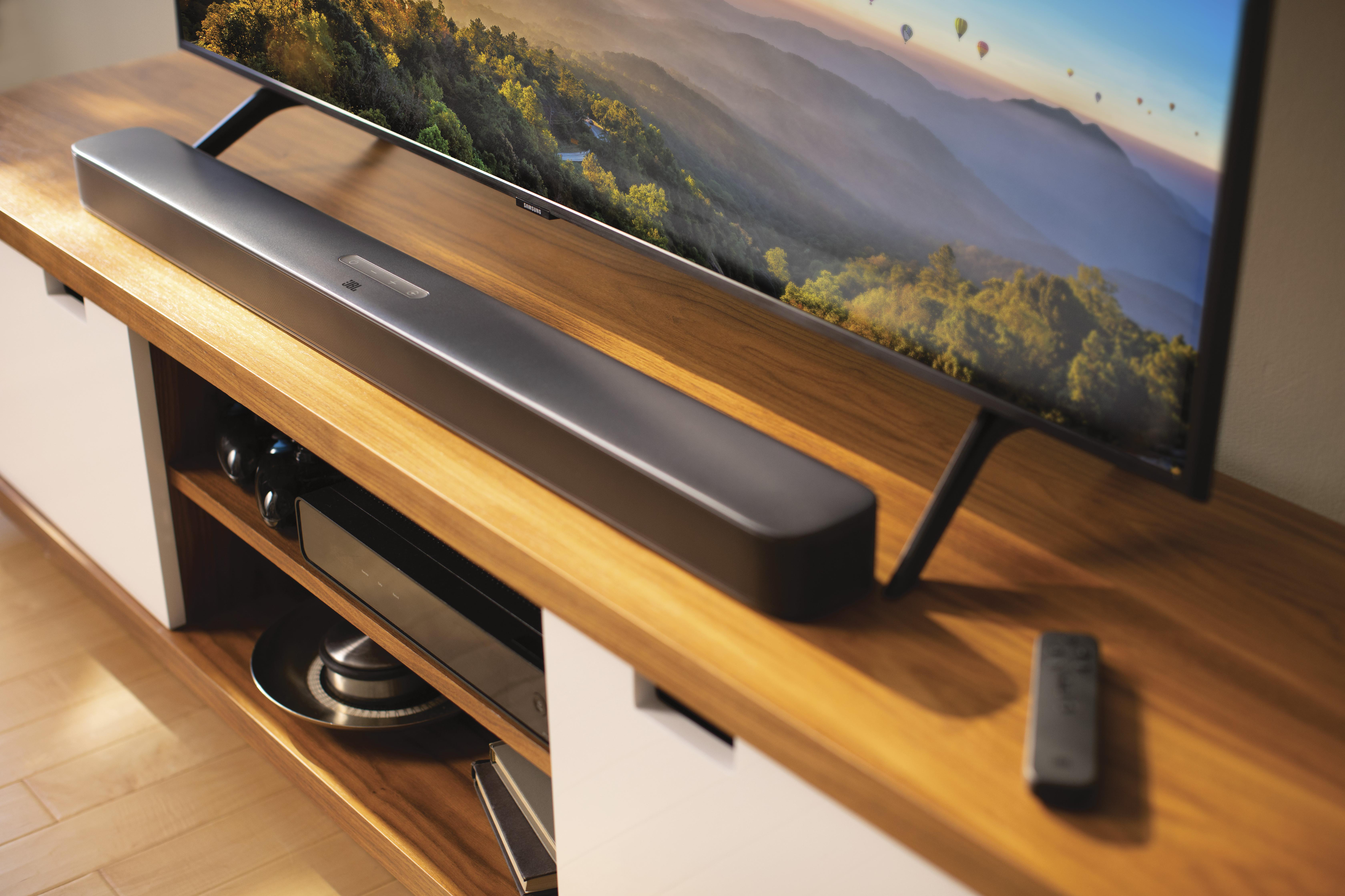 Eine schwarze Soundbar befindet sich auf einem Holzschrank, darüber ein Fernseher. Eine Fernbedienung liegt auf dem Schrank.