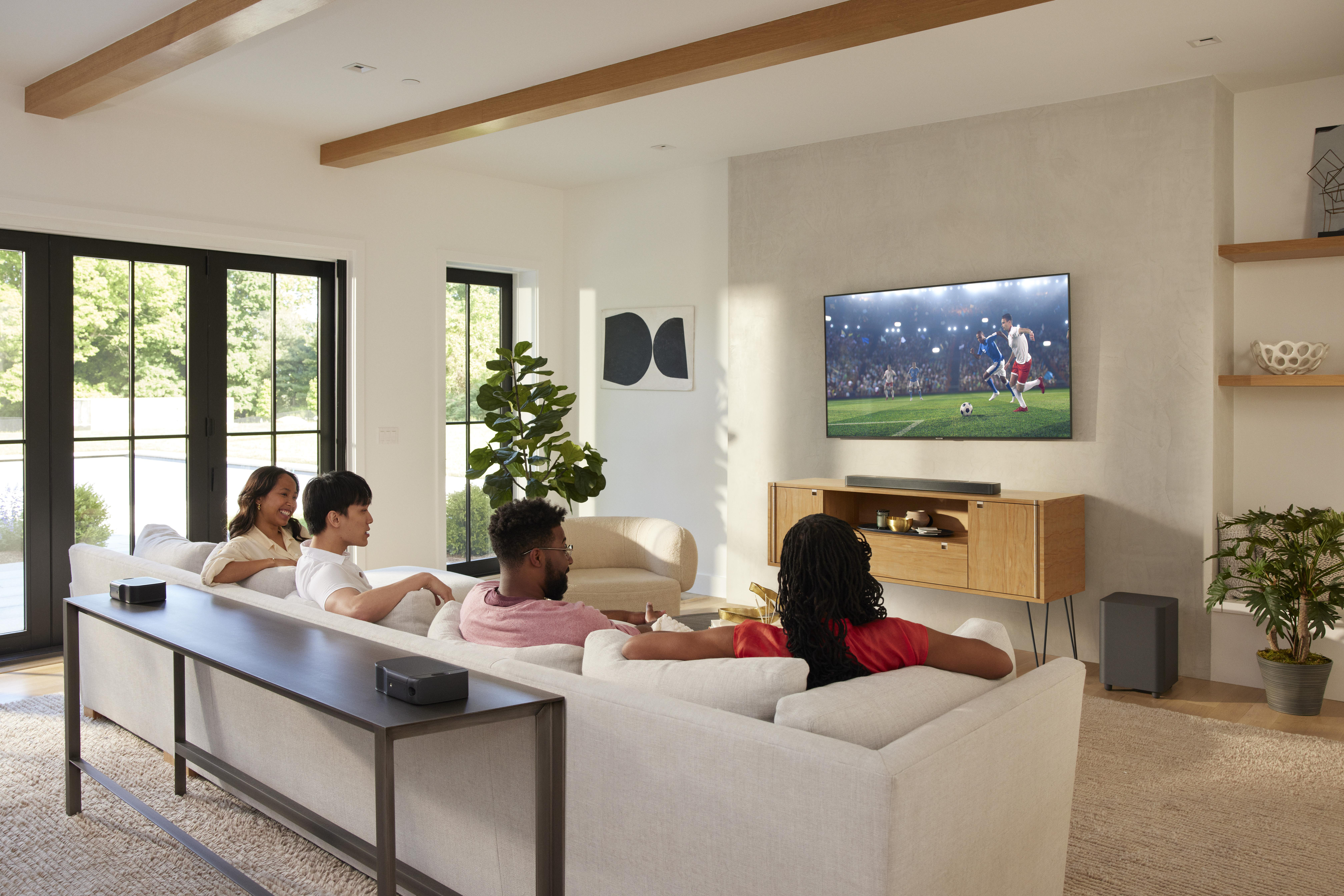 Gruppe von Leuten schaut Fernsehen in modernem Wohnzimmer. Fernseher ist auf Holzschrank montiert.