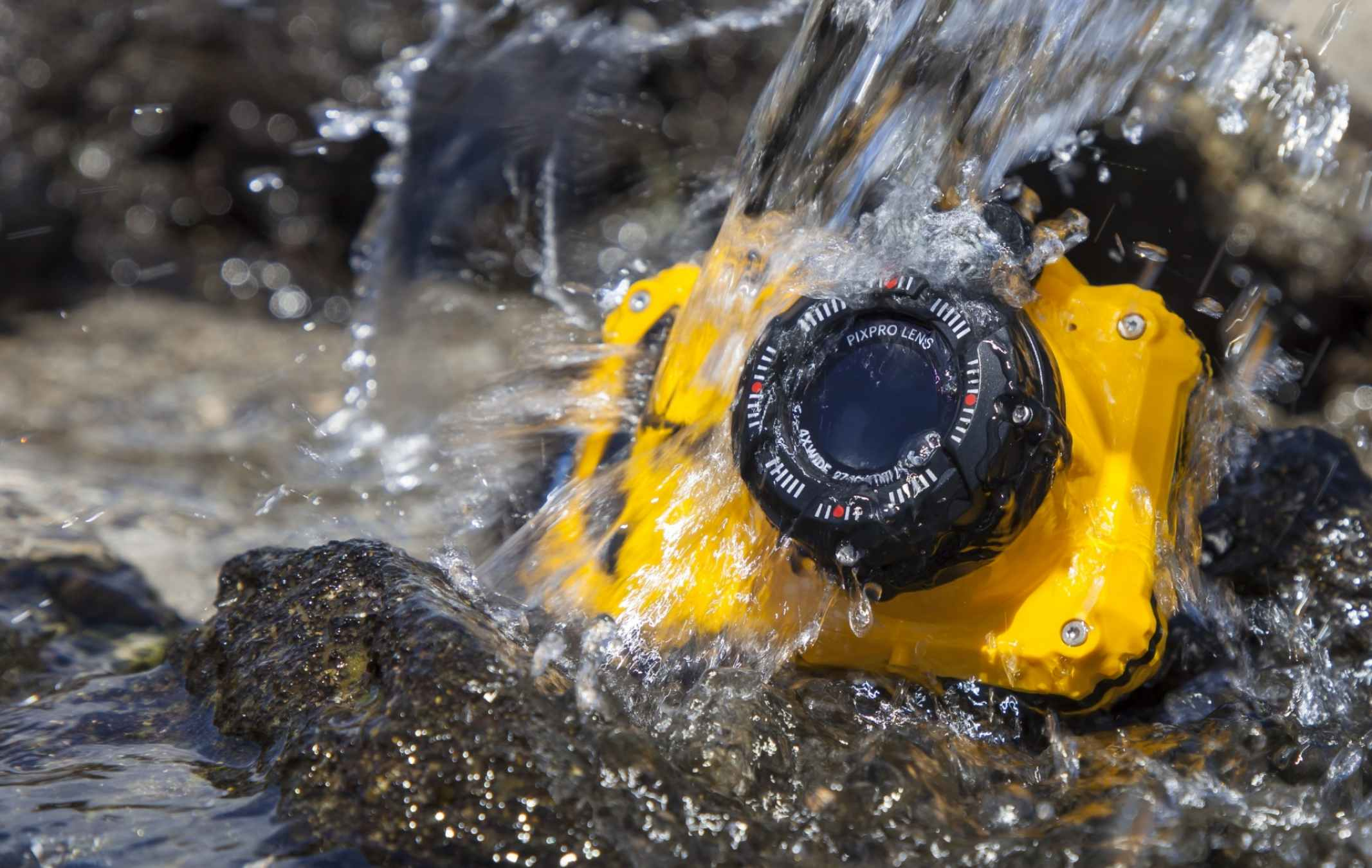 Gelbe wasserdichte Kamera im Wasser, Wasser spritzt auf Felsen.