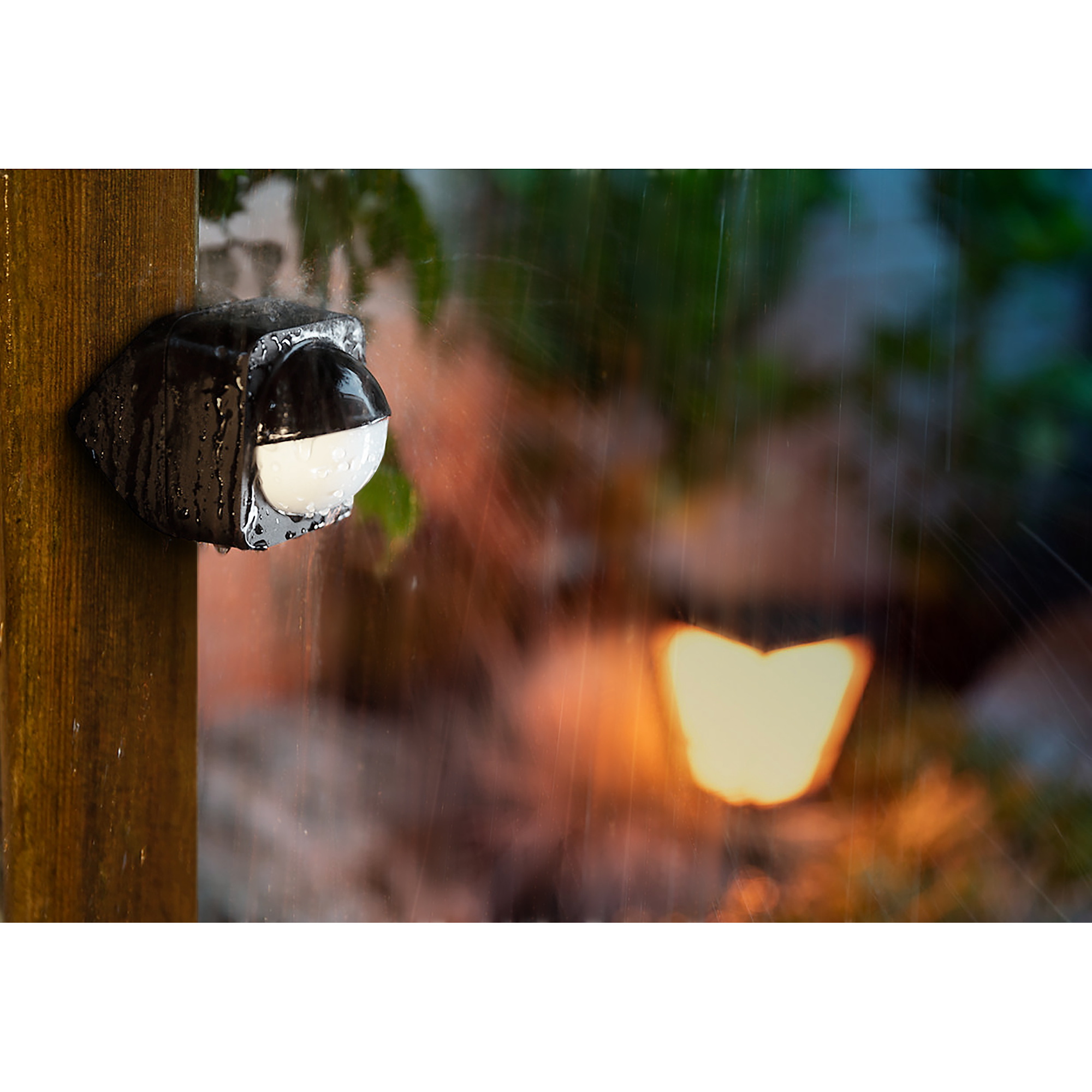 Una lámpara exterior negra sujeta a un poste de madera, con lluvia.