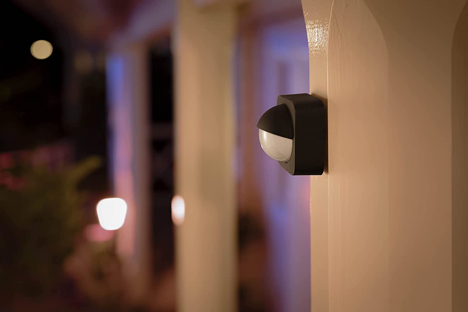 Luminaria exterior negra en columna beige, fondo nocturno borroso.