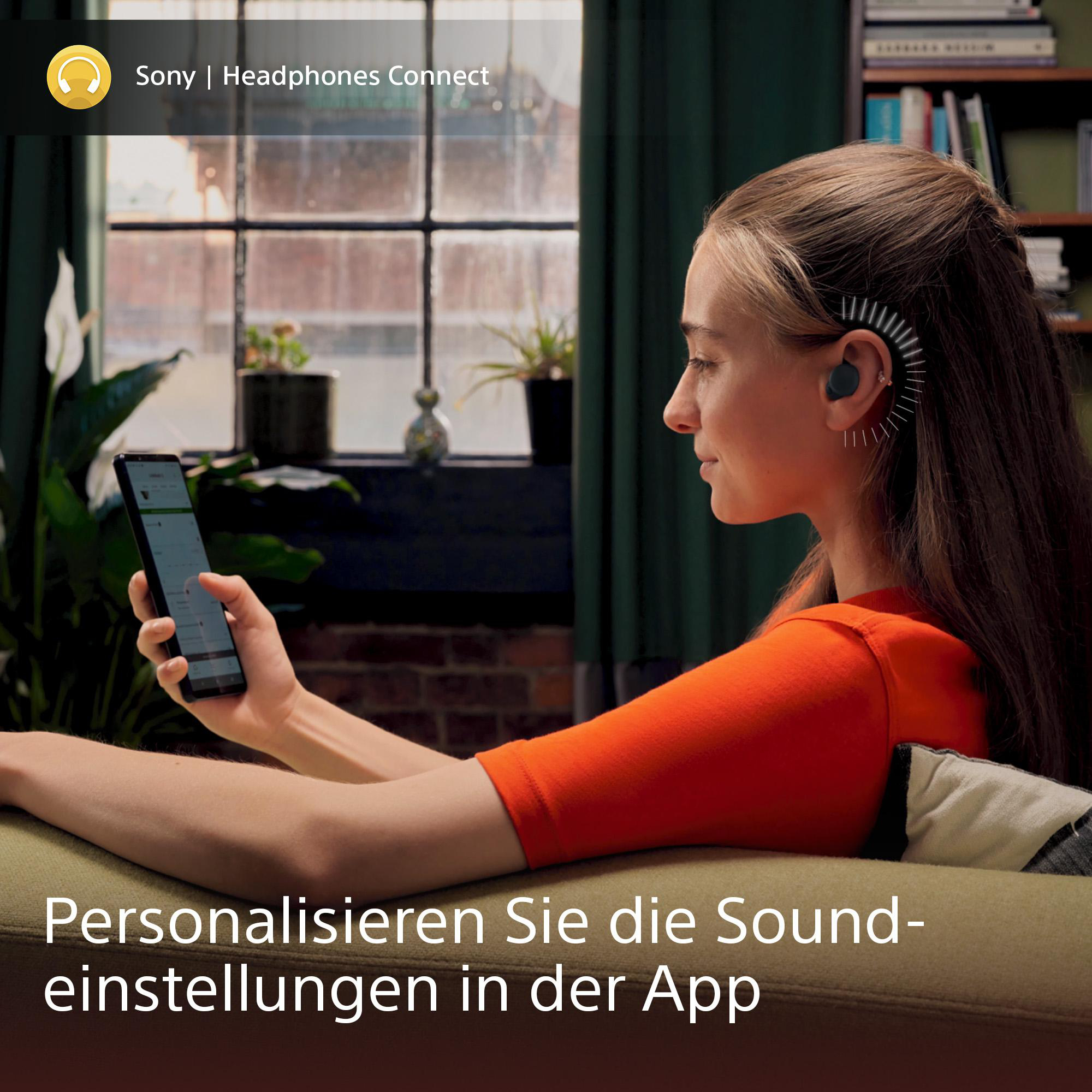 Frau mit Kopfhörern schaut auf das Telefon. Text auf dem Bildschirm. Pflanze im Hintergrund.