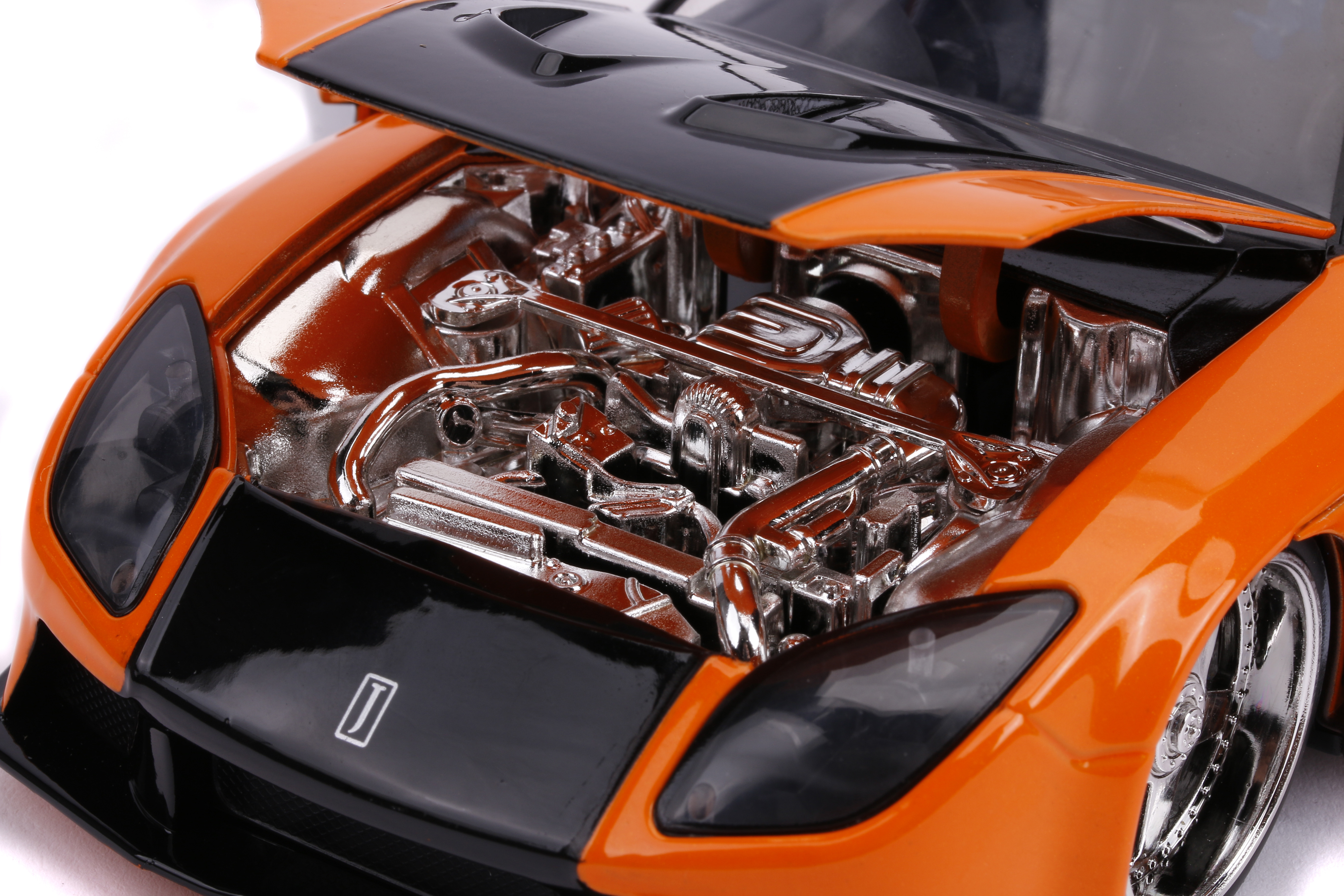 Orangenes Spielzeugauto mit schwarzer Motorhaube, offen, um Chrommotor zu zeigen. Räder sichtbar.