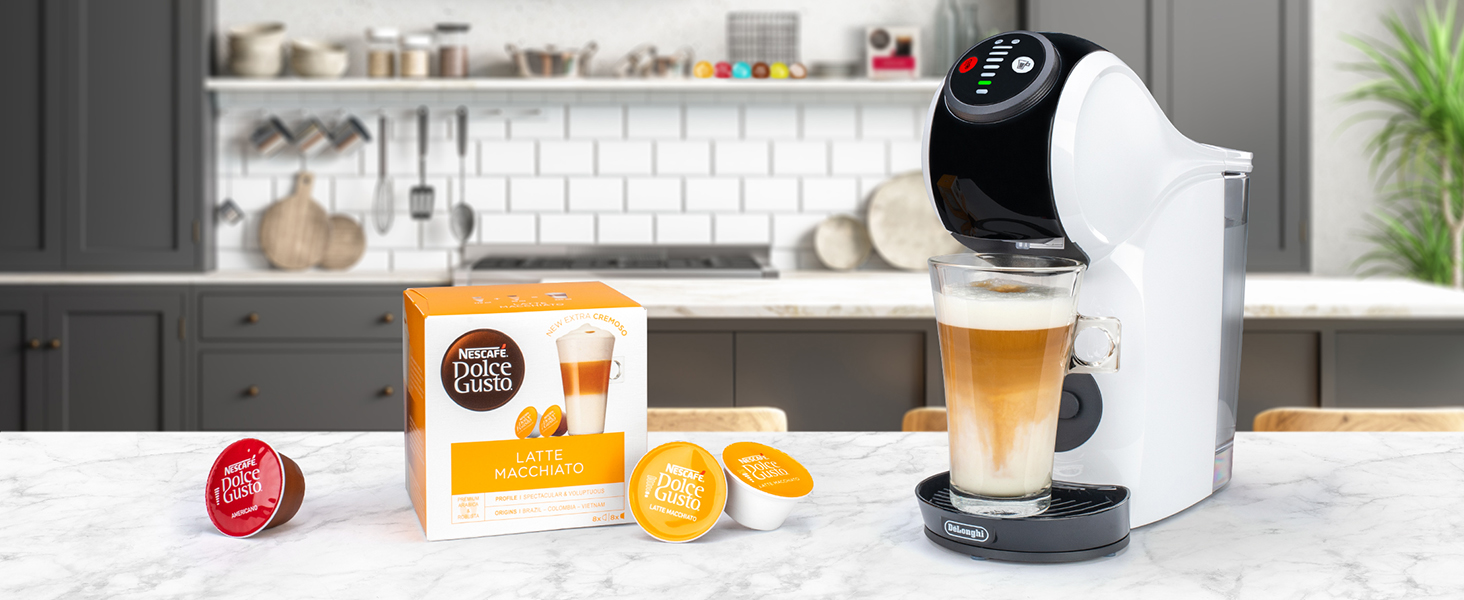 Una cafetera preparando latte macchiato, con cápsulas de café y una caja sobre una superficie de mármol.