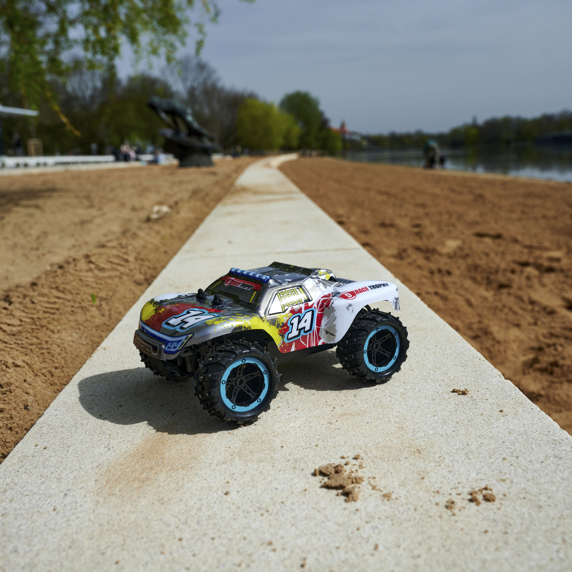 Ferngesteuertes Auto auf Betonoberfläche. Sandstrand und Wasser im Hintergrund.