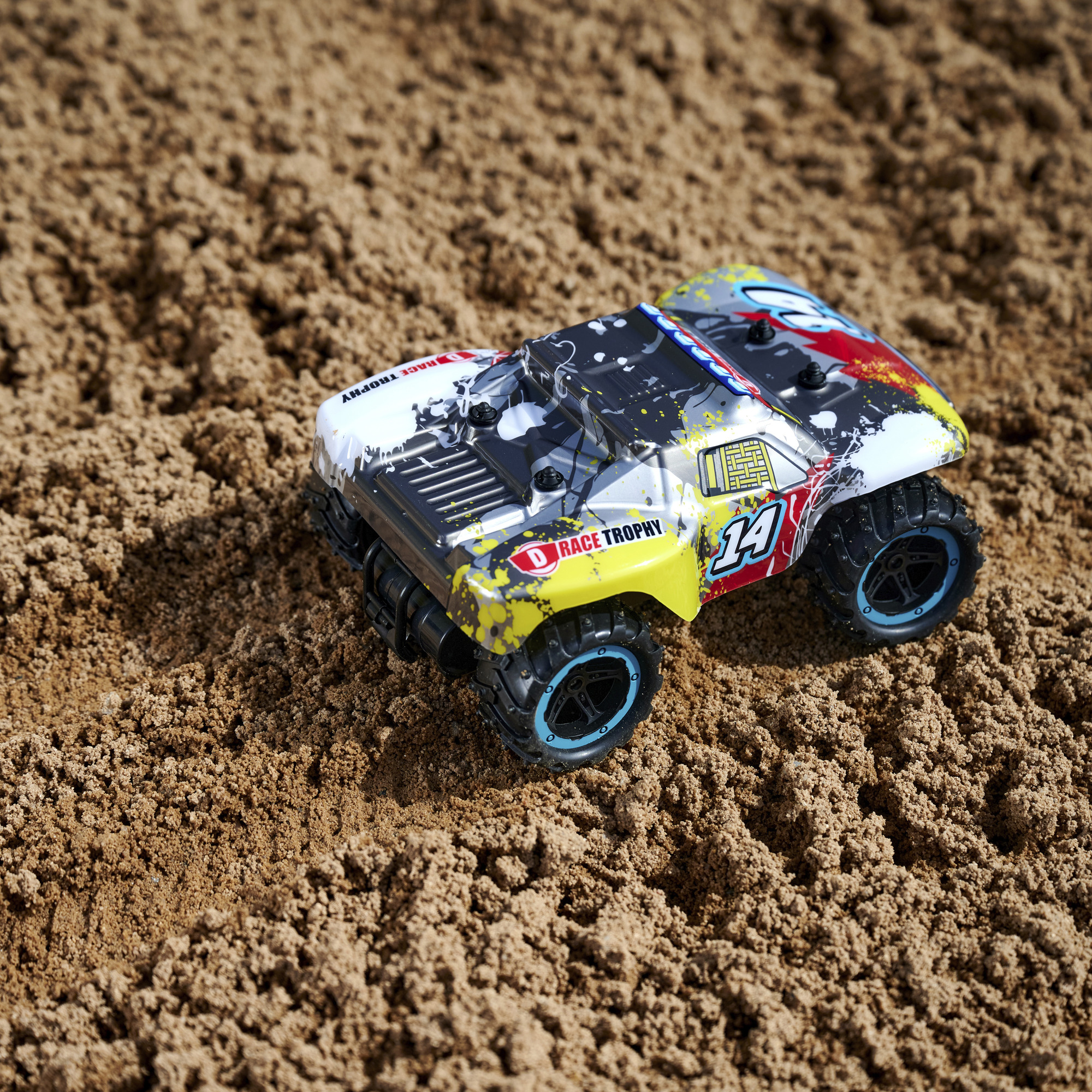 Kleines Spielzeugauto auf Sand, mit Rennpokal-Design.
