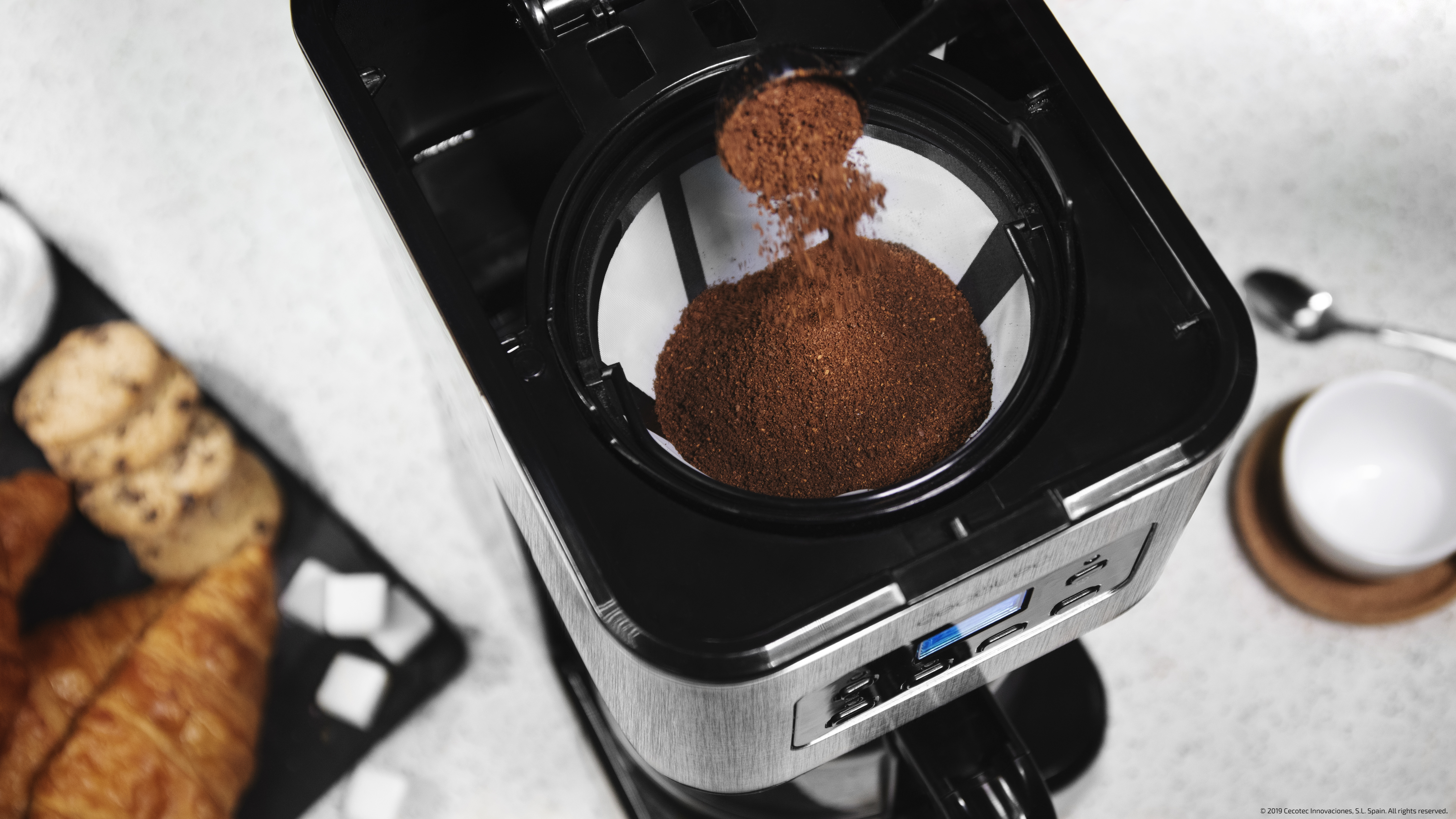 Una cafetera con café molido vertiéndose. Hay pasteles y galletas alrededor.