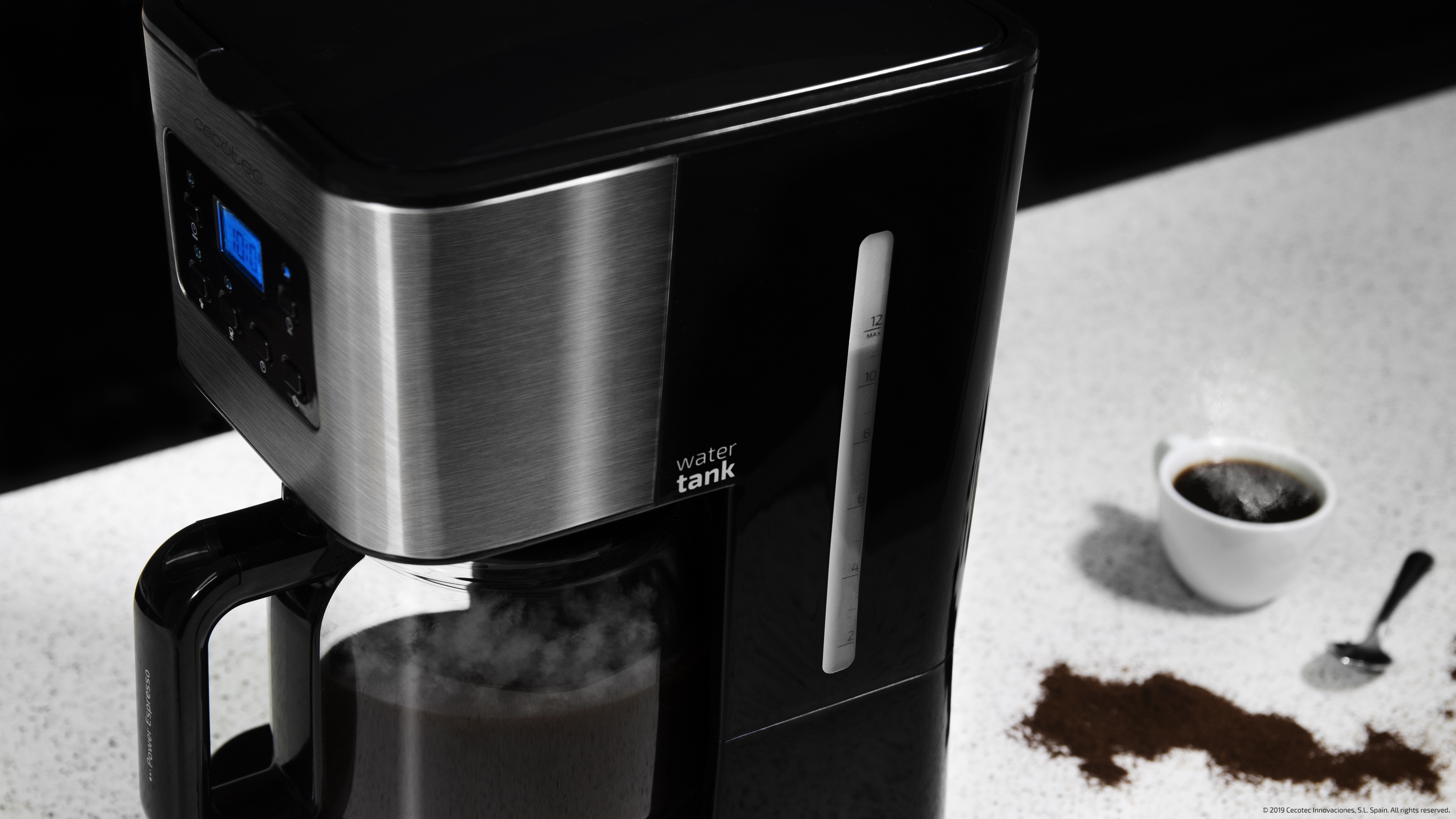 Cafetera negra con detalles de acero inoxidable. Una taza de café y posos a un lado.