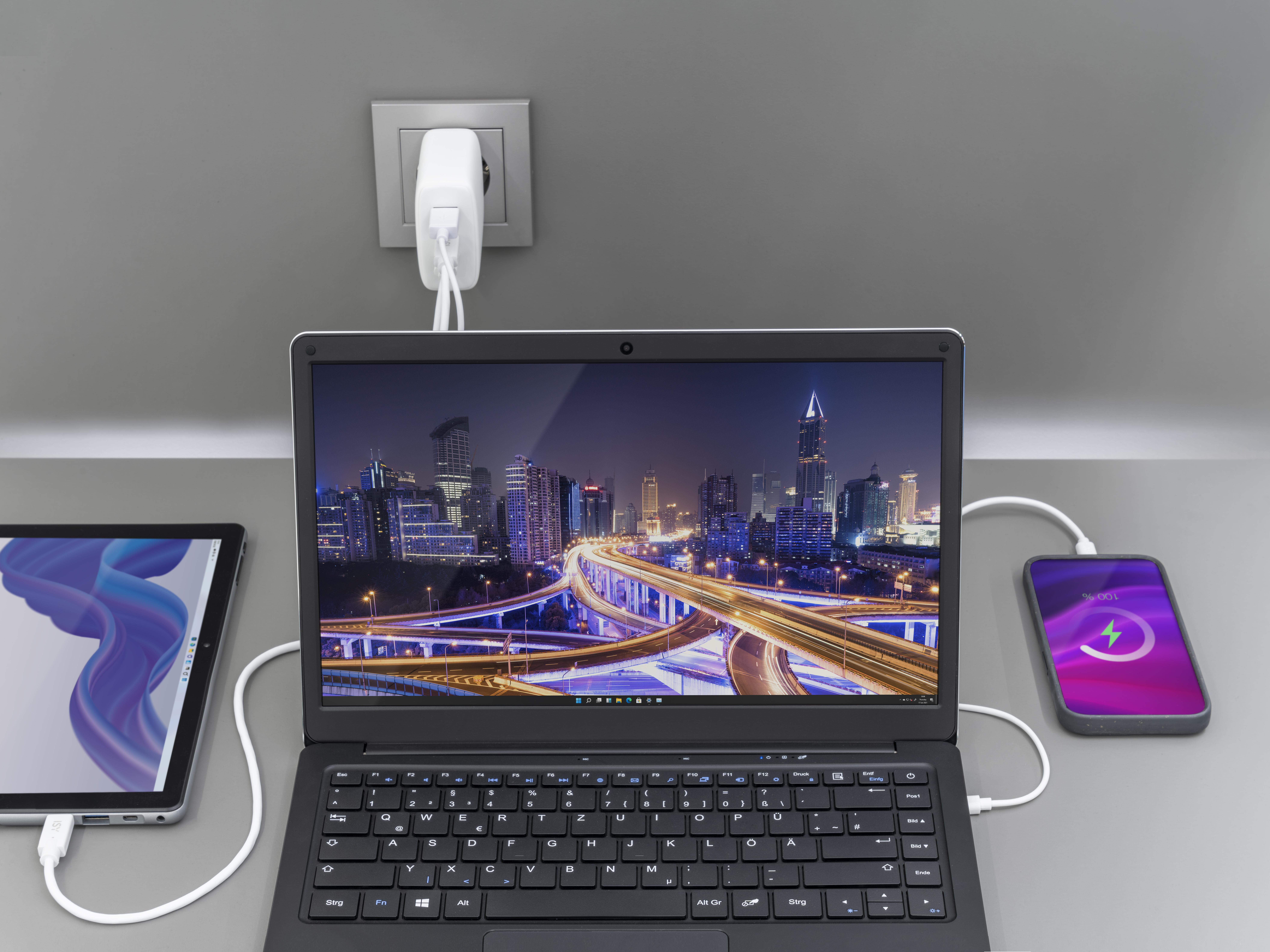 Laptop, Tablet und Telefon laden gleichzeitig auf grauer Oberfläche.