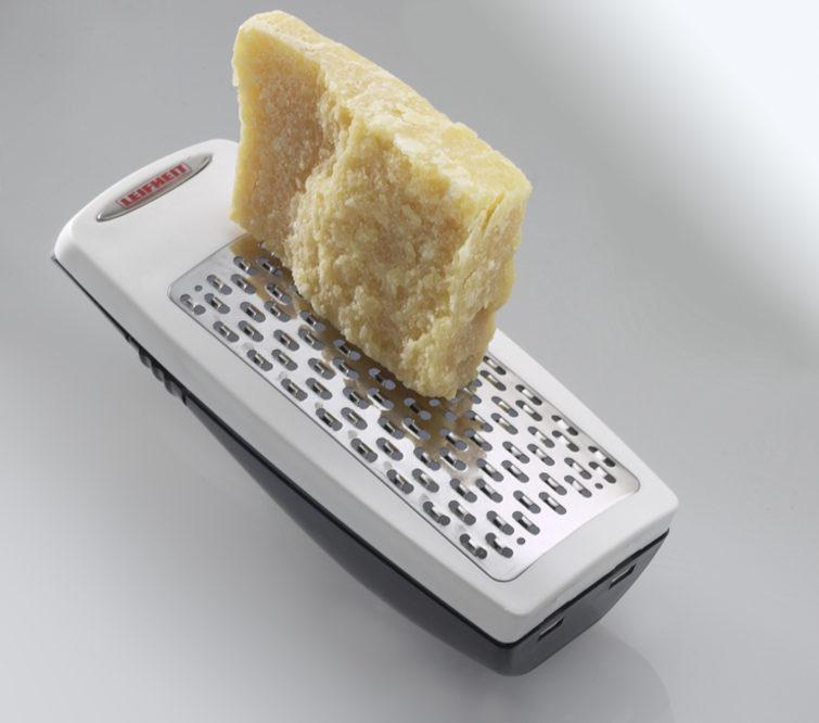 Käsereibe mit einem Stück Käse auf weißer Oberfläche.