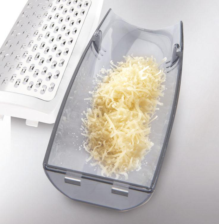 Nahaufnahme eines Reibeisens und geriebenem Käse. Geriebener Käse in einem transparenten Behälter.