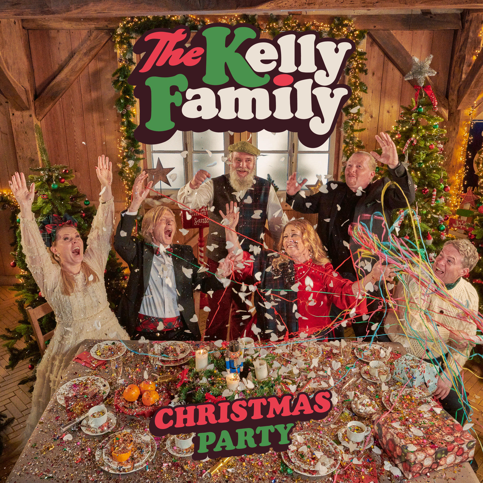 Image de The Kelly Family célébrant Noël. Ils sont réunis autour d'une table avec des confettis et des décorations.