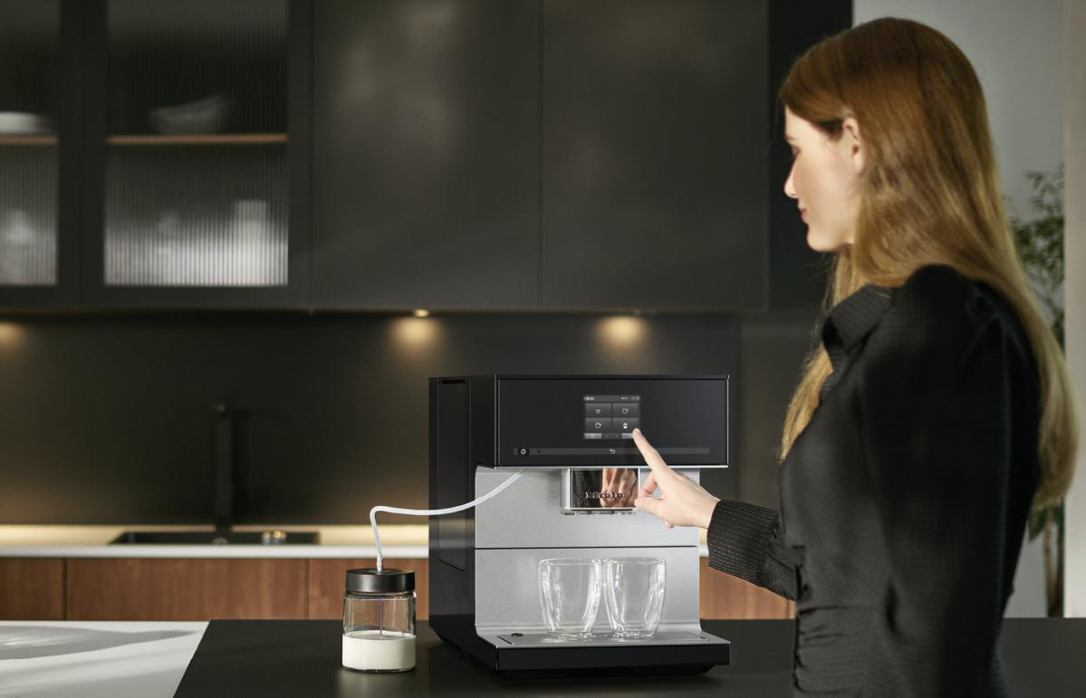 Frau benutzt Kaffeemaschine, schwarz und silber, zwei Gläser, Milchbehälter, Küche.
