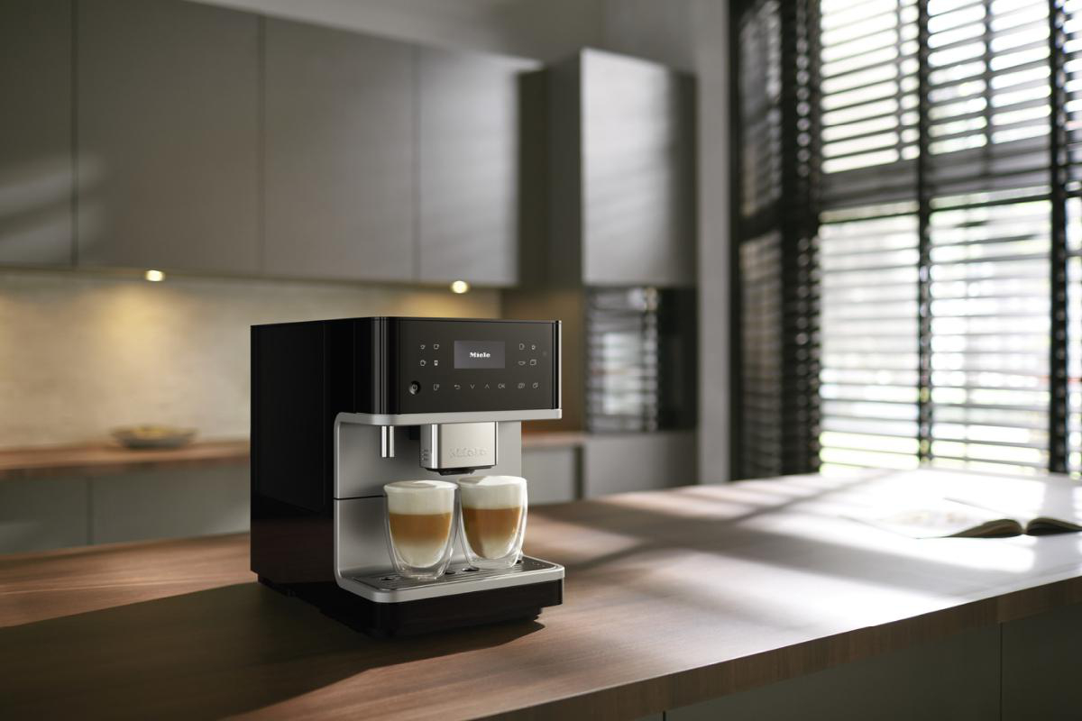 Schwarze und silberne Kaffeemaschine mit zwei Kaffeegläsern auf einer Holztheke.