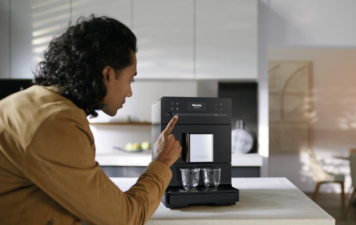 Eine Person berührt den Bildschirm einer schwarzen Kaffeemaschine.