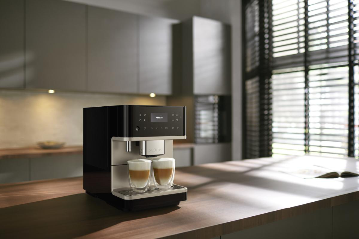 Eine schwarz-silberne Espressomaschine auf einer Holz-Arbeitsplatte, mit zwei Gläsern Latte.