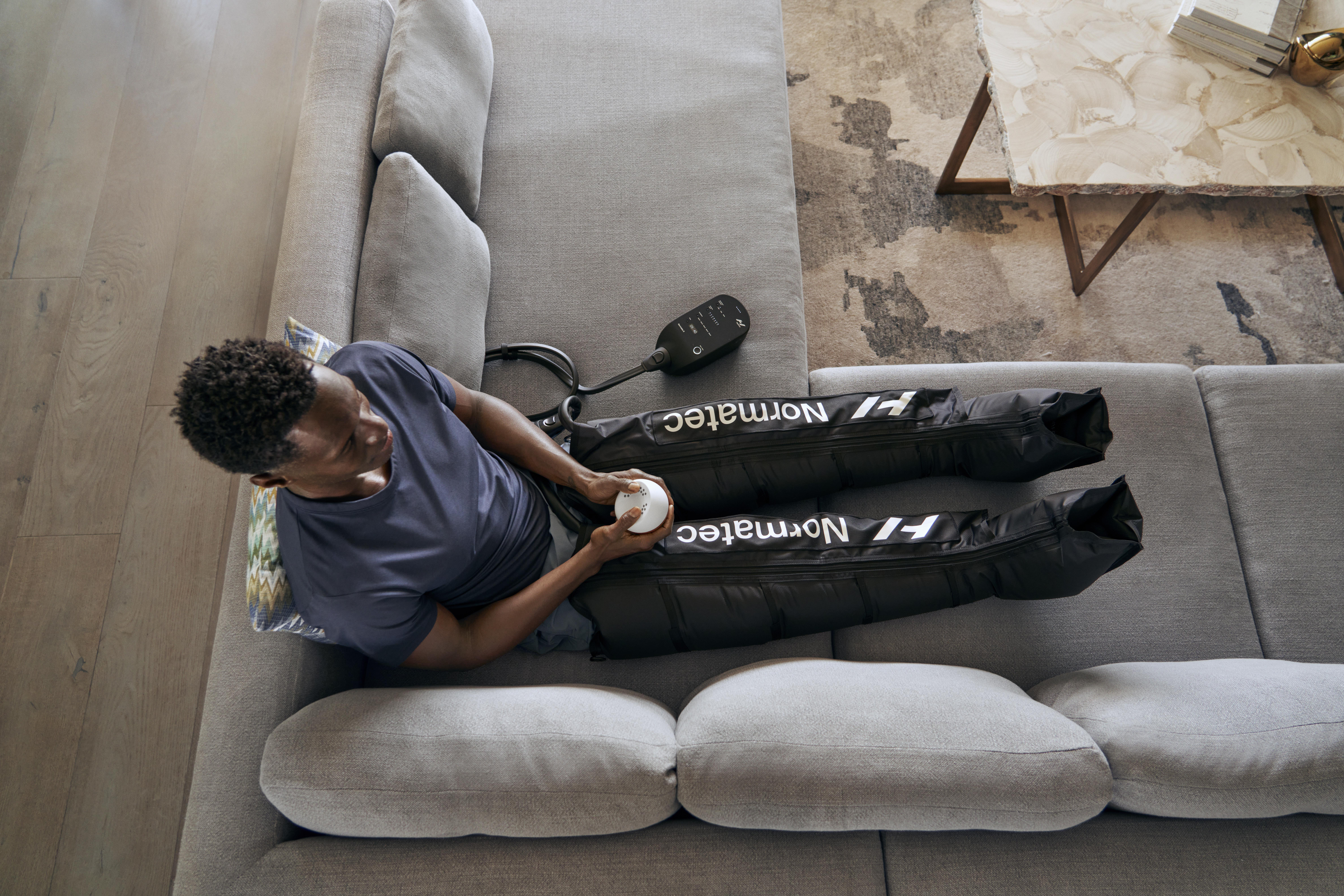 Mann benutzt Normatec Bein-Erholungssystem auf einer Couch.