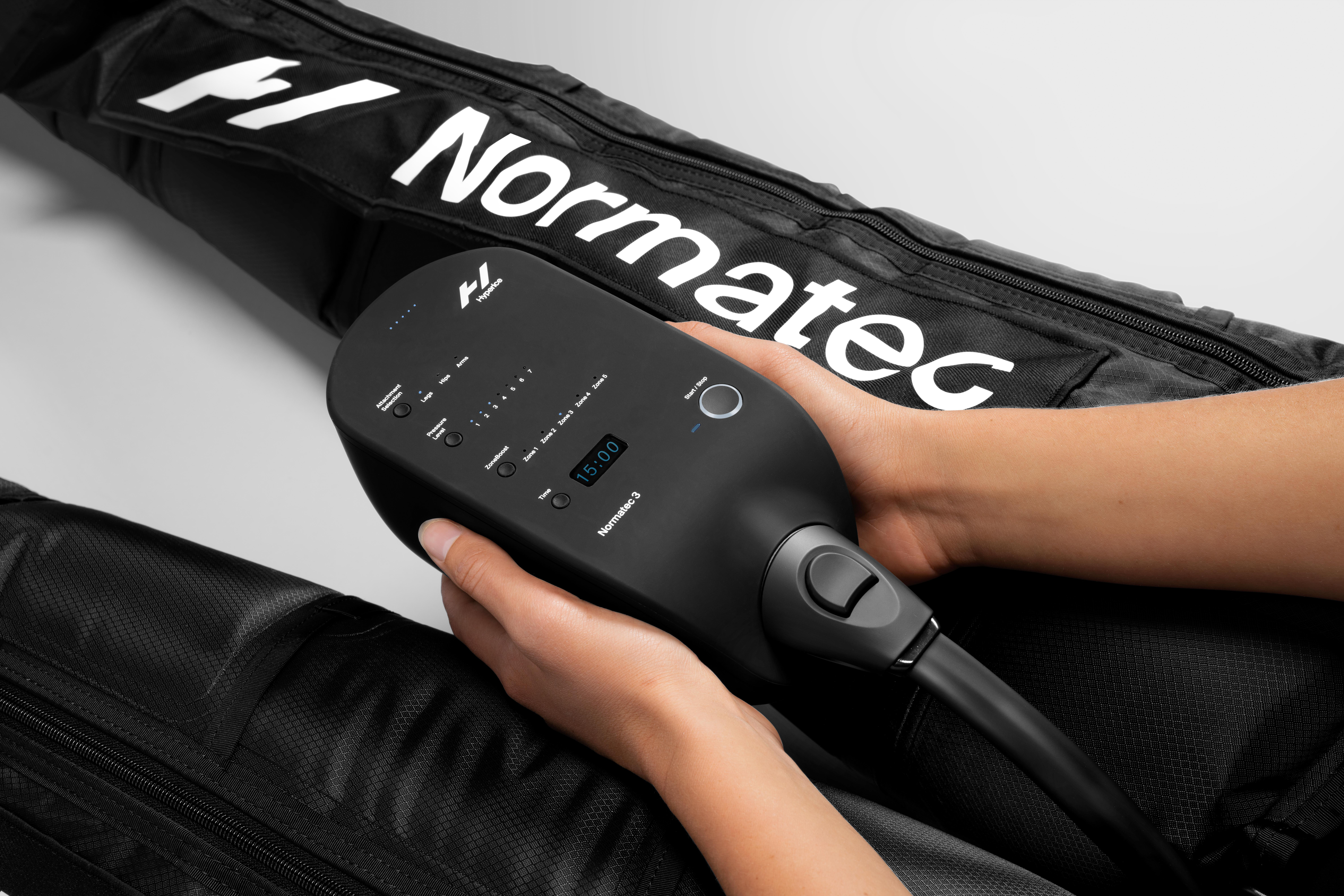 Hände halten ein schwarzes Normatec 3-Gerät neben schwarzen Kompressionsärmeln.