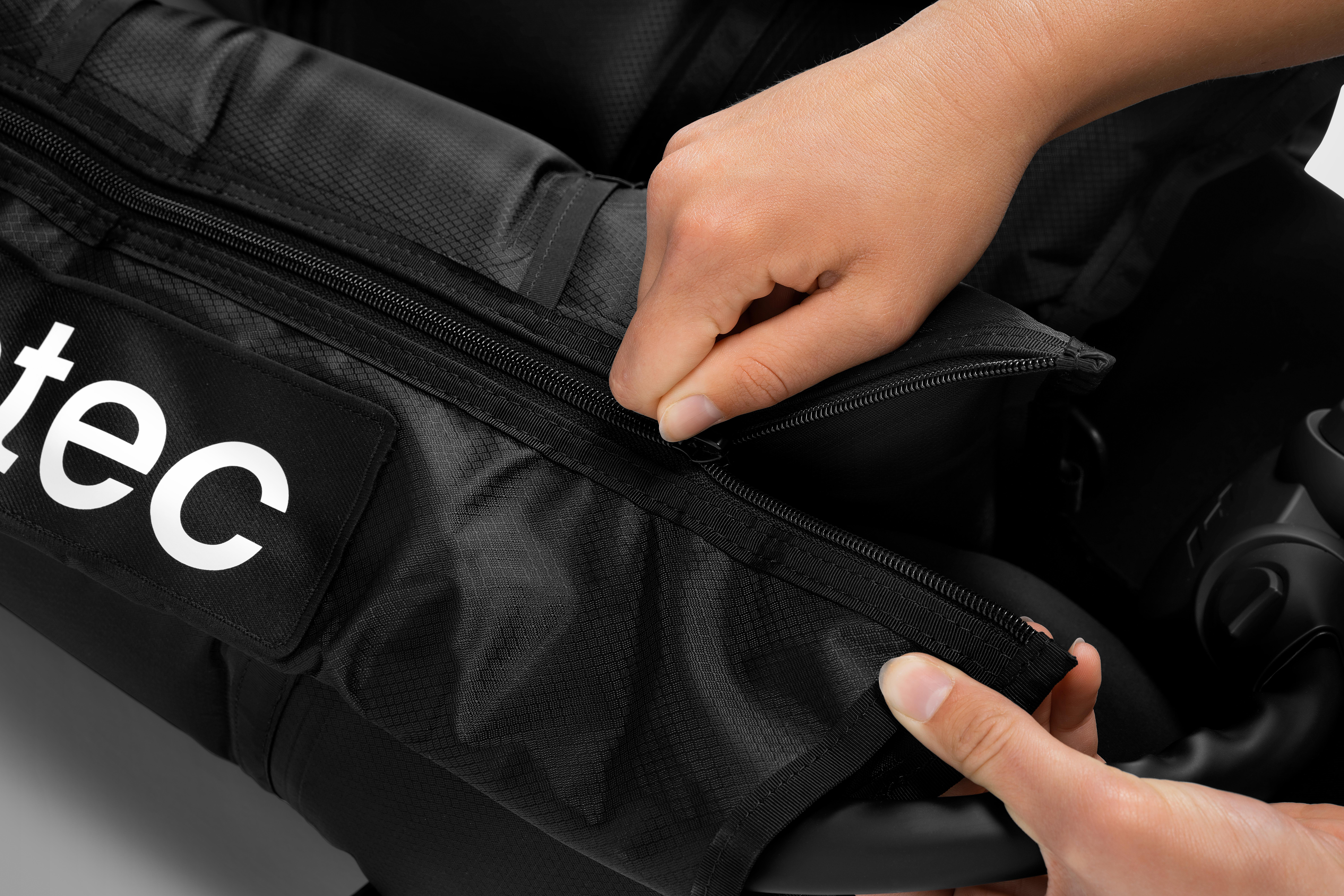 Hände, die eine schwarze Tasche zumachen. Auf der Tasche steht das Wort 'tec' in Weiß.