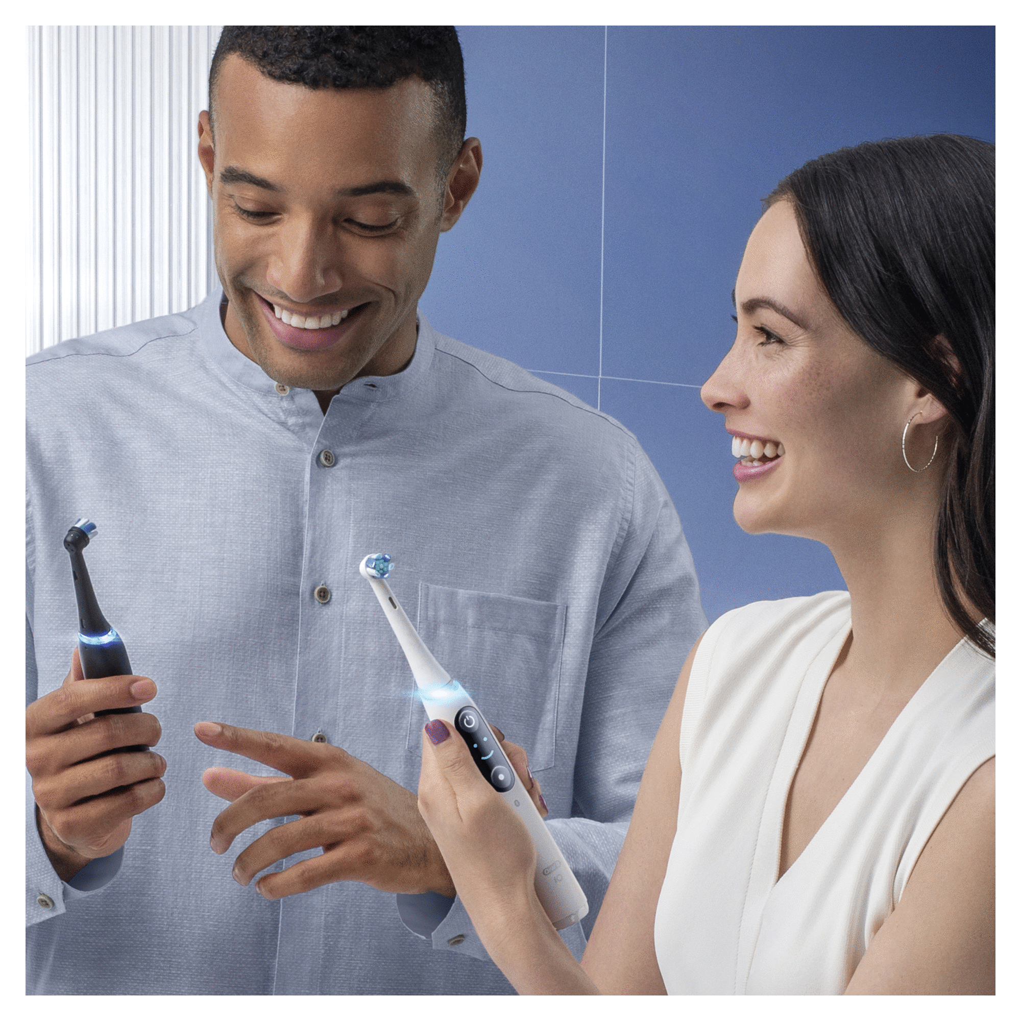 Man and woman using electric toothbrushes, smiling. White background.