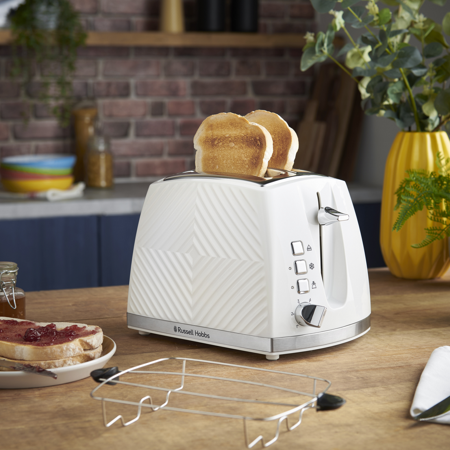 White toaster with two slices of toast. A metal rack and a plate with toast.