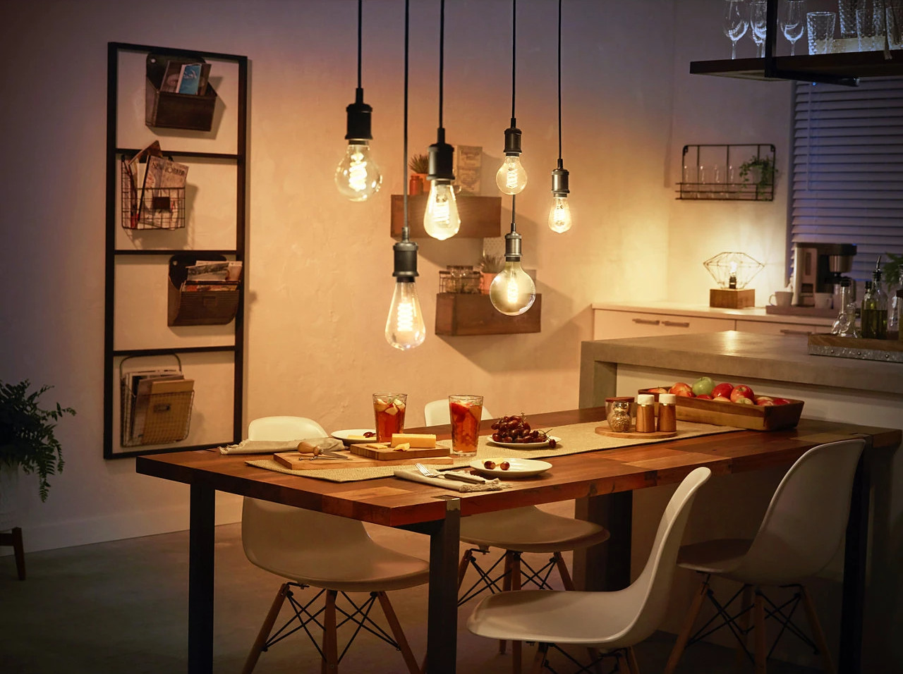 A dining room with a wooden table, light bulbs hanging, and food on the table.