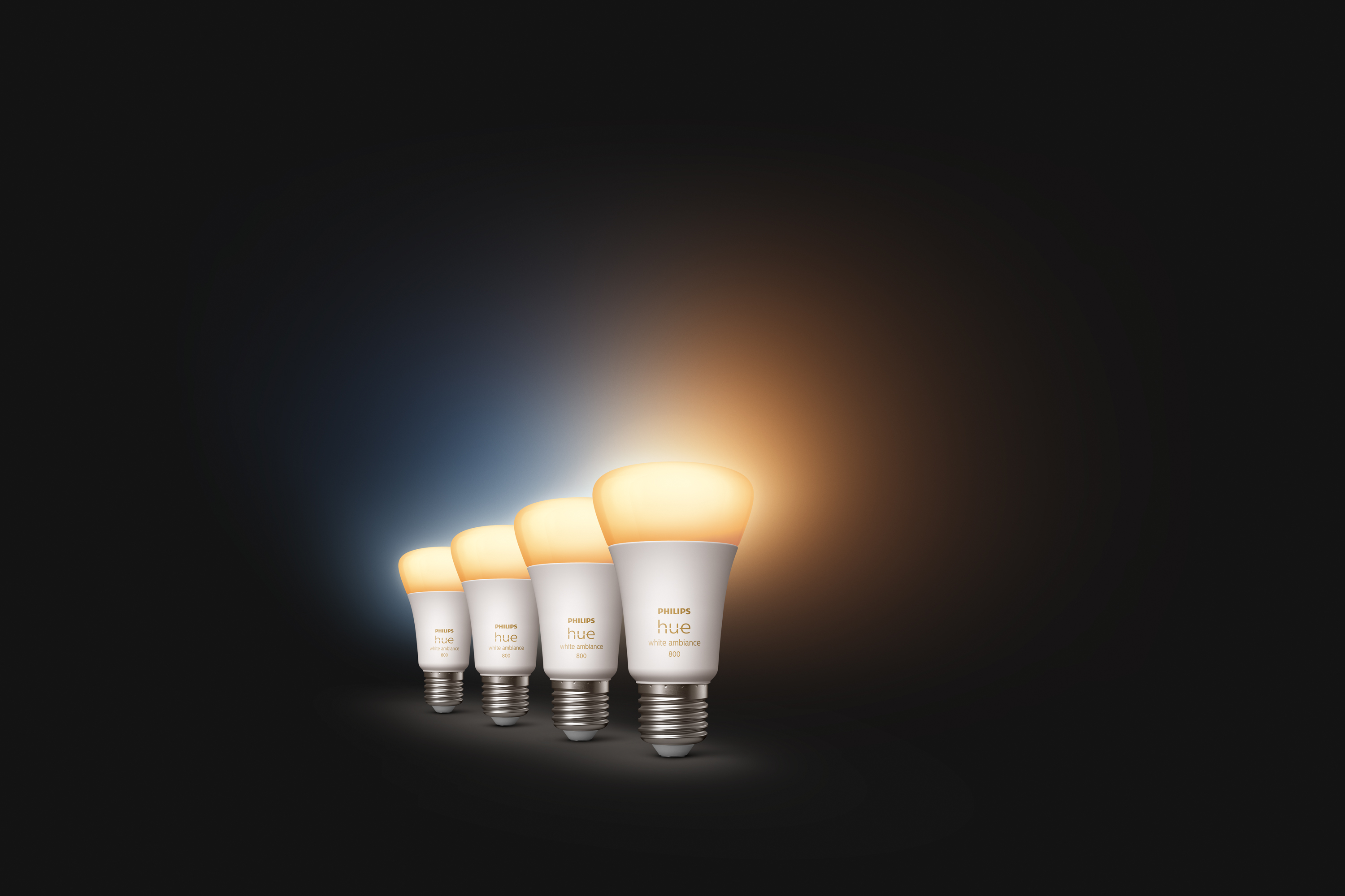 Vier Philips Hue-Glühbirnen leuchten auf. Der Hintergrund ist dunkelblau bis orange.