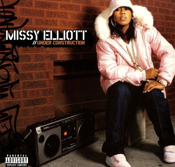 Missy Elliott rózsaszín kabátban és sapkában, egy téglás fal mellett ül egy boombox-szal. Album borító, "Under Construction".