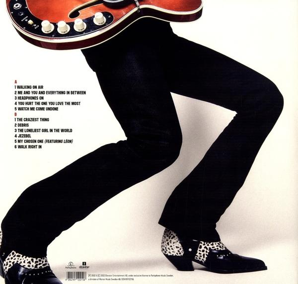 Ein Mann in schwarzer Hose und Schuhen mit Gitarre. Text eines Musikalbums links.