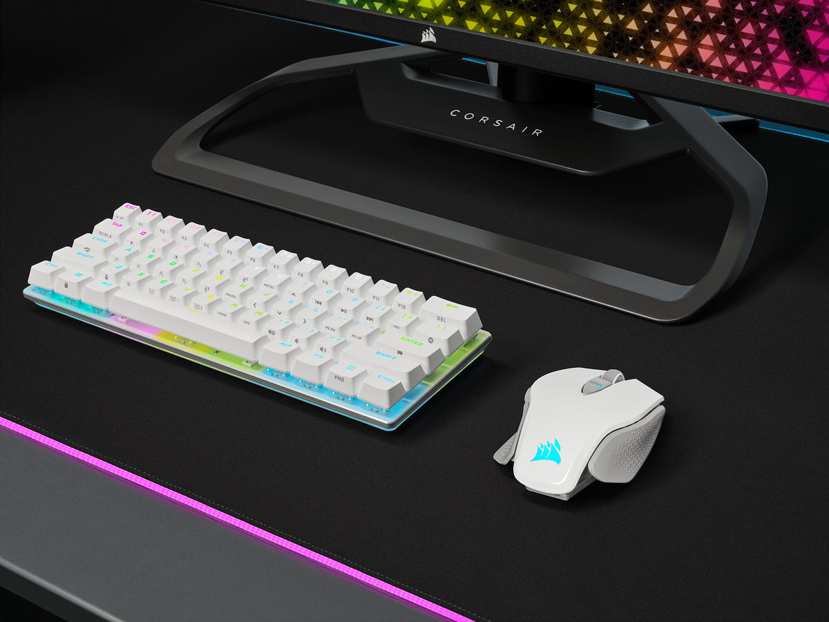 Eine weiße Tastatur und Maus auf einem schwarzen Schreibtisch, mit einem Monitor im Hintergrund.