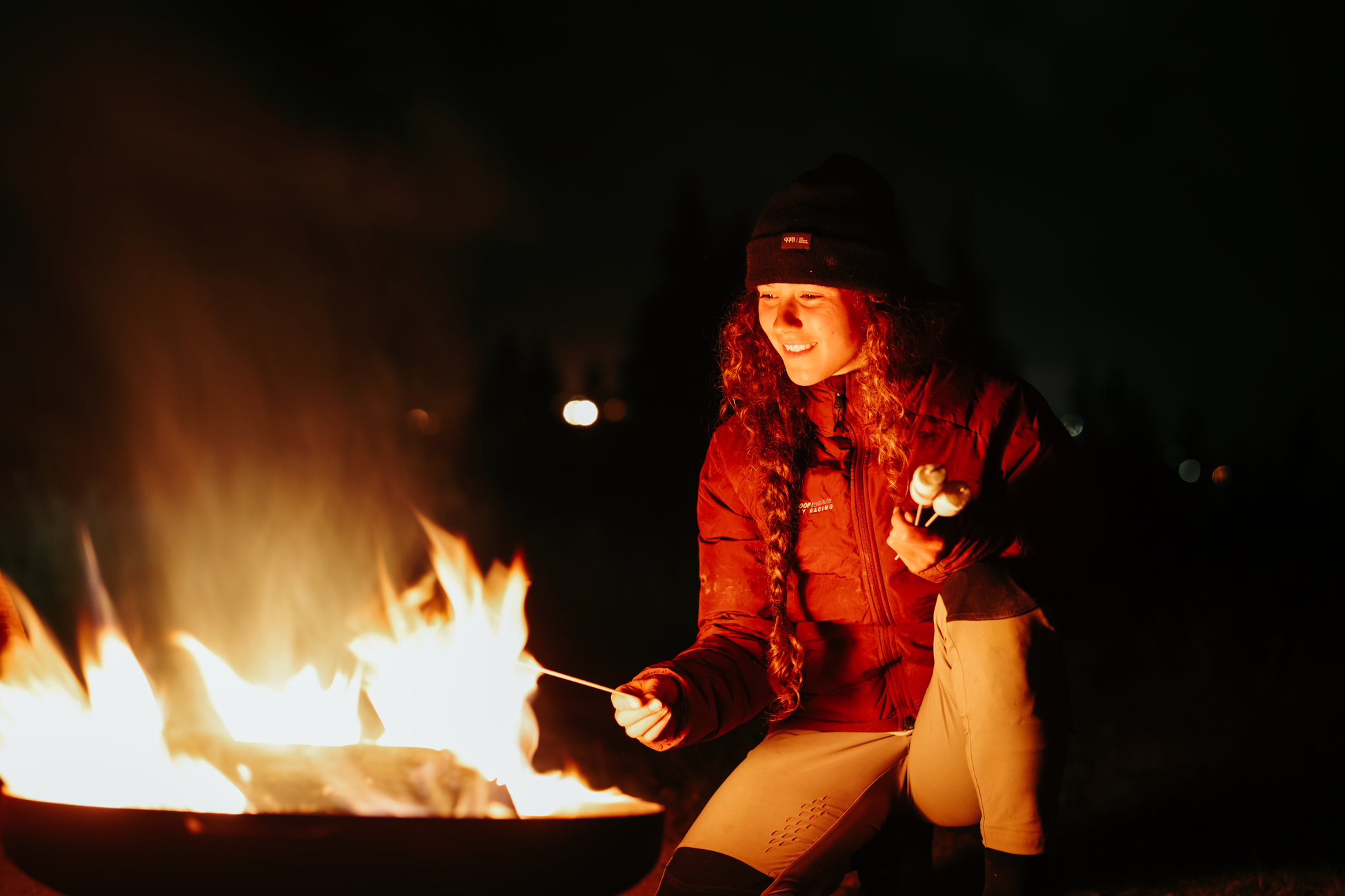 Frau vor Feuer, die Marshmallows in der Nacht röstet. Dunkler Hintergrund.