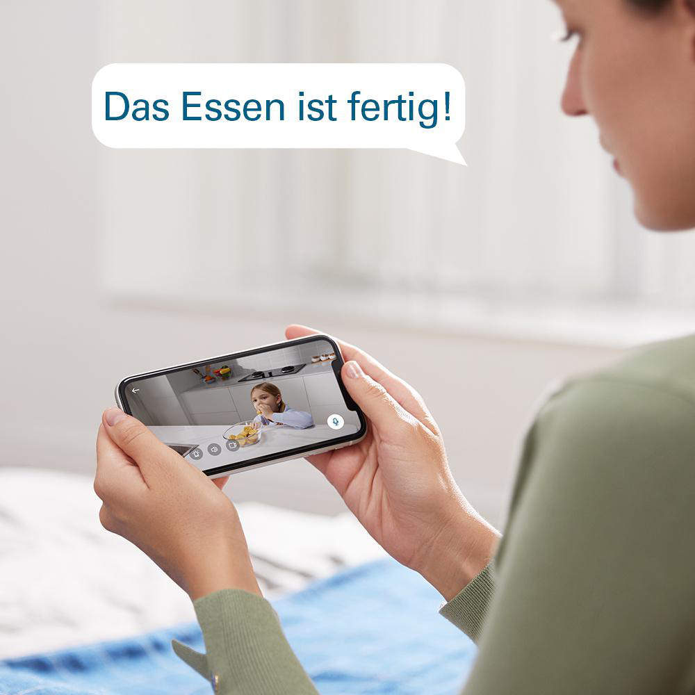 Frau hält Handy mit Kind beim Essen. Sprechblase sagt 'Das Essen ist fertig!'
